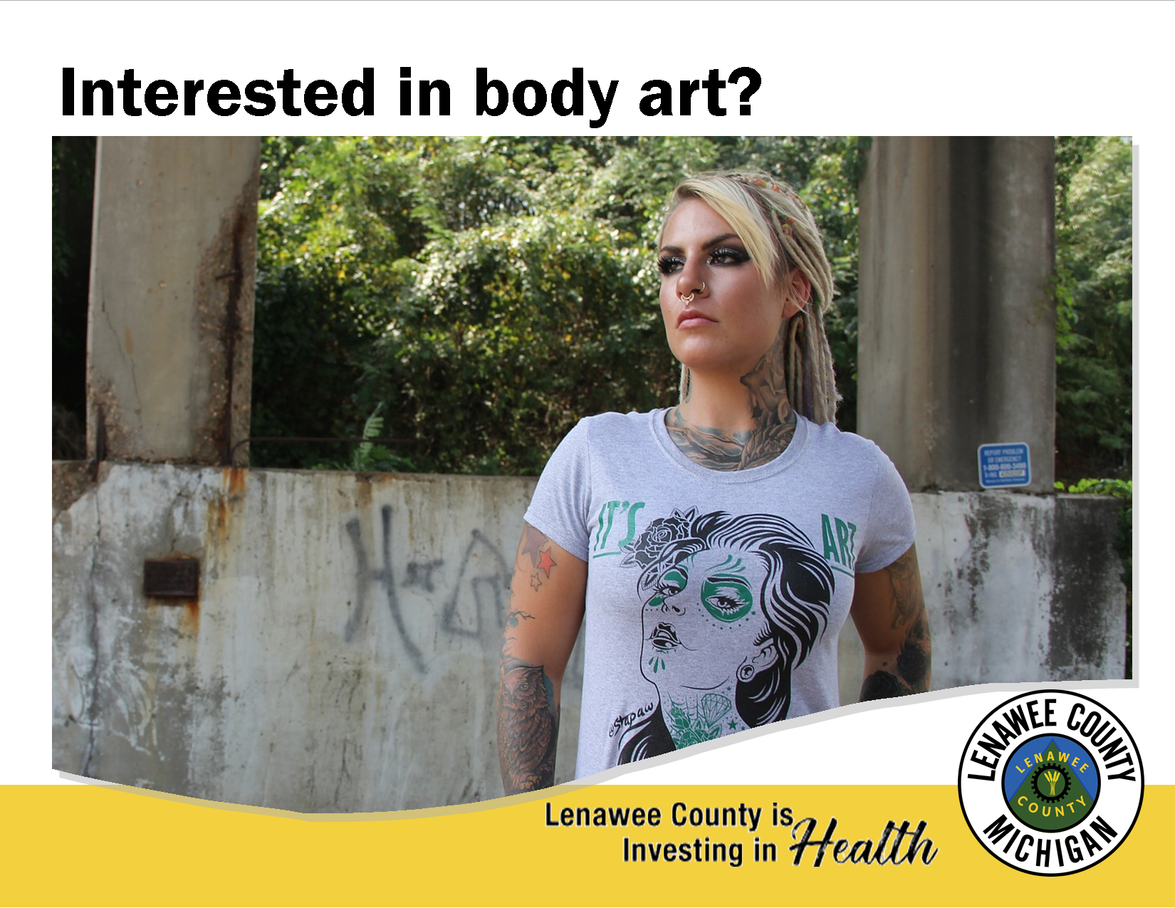 Blonde girl with tattoos and piercings casually standing in front of graffitti wall with tshirt stat